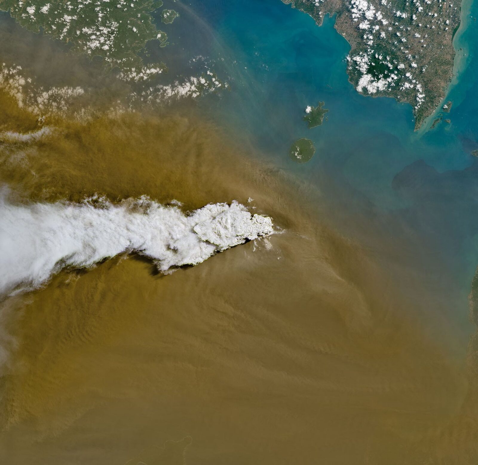 Satellite view of a white plume of volcanic gas and a broad brown ash cloud spreading over the sea from Anak Krakatau.