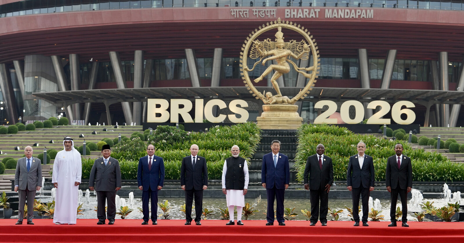 The official group photograph of heads of delegation standing in front of a BRICS 2026 sign at Bharat Mandapam, New Delhi.