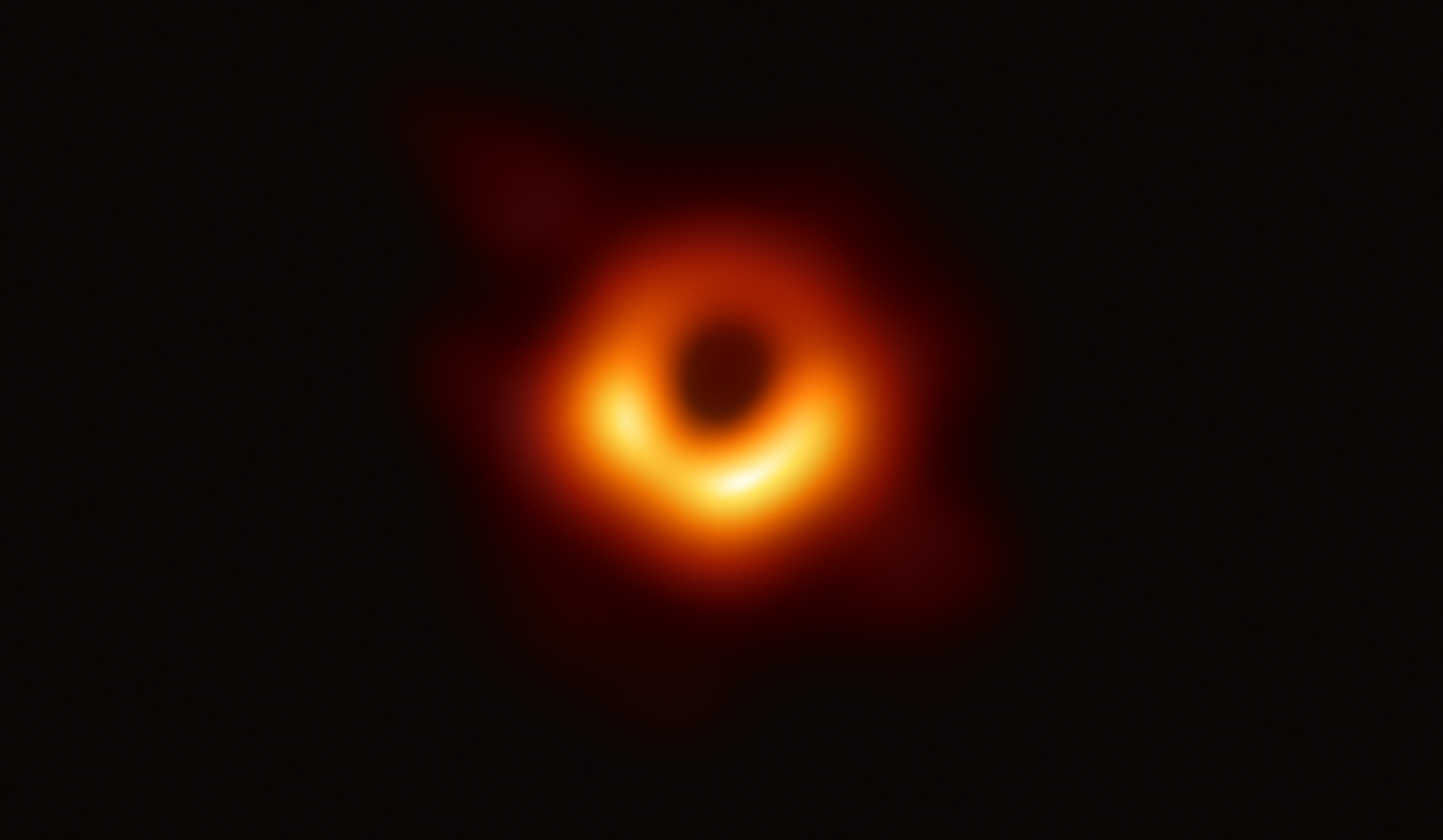 Orange ring surrounding the dark central shadow in the EHT image of M87.