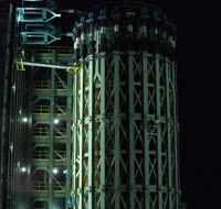 A very tall white tank inside a steel test frame; water bursts from its side.